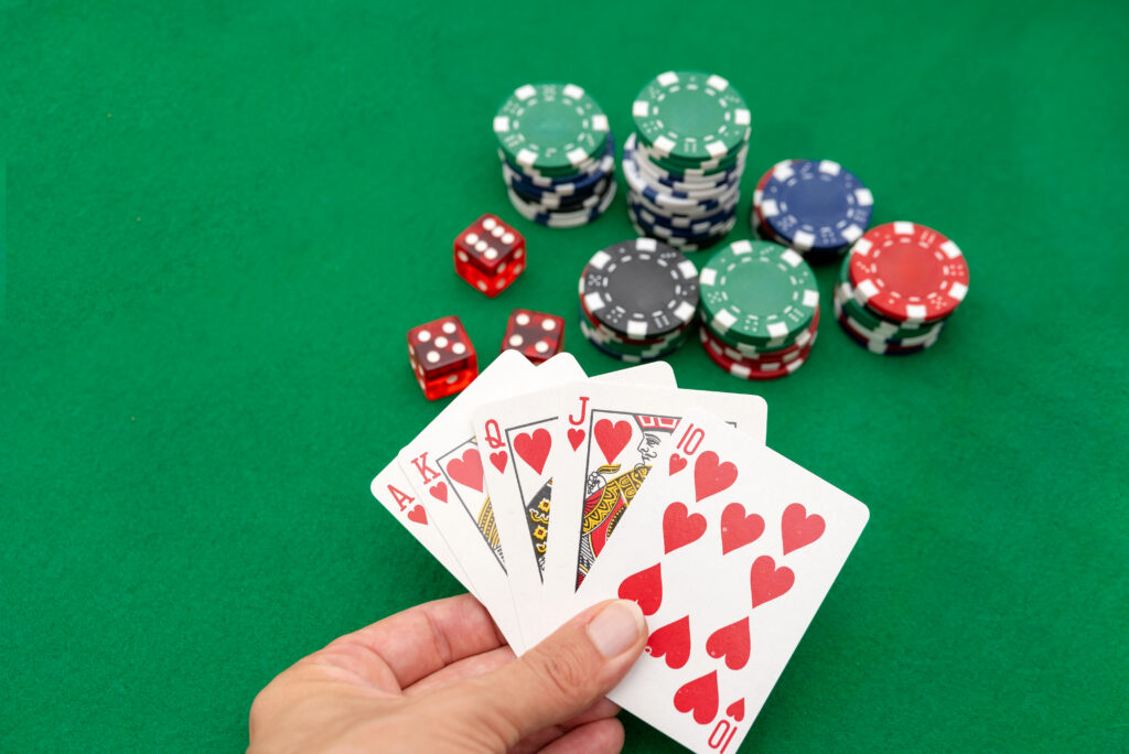 Four playing cards with hearts and poker chips on a green felt surface